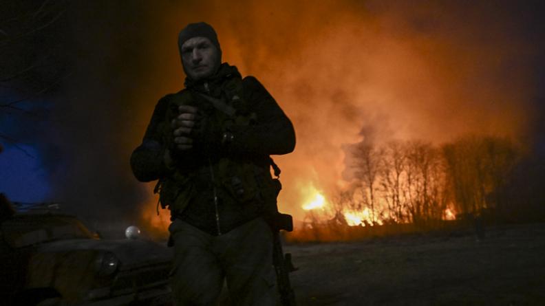 Un militaire ukrainien monte la garde près d'un entrepôt en flammes après un bombardement russe. 