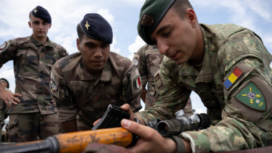 Un soldat roumain et un soldat français échangent autour de leur armement respectif..